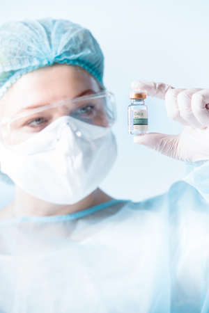 Close up view of doctor with an ampule of covid vaccine on blue backの写真素材