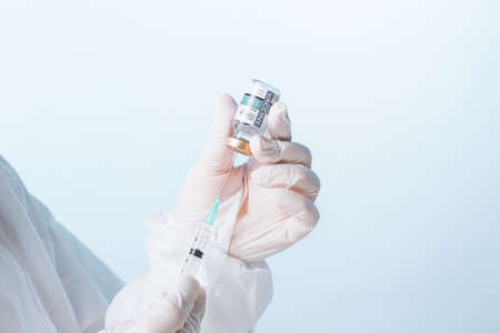 Close up view of doctorâs hands with an ampule of covid vaccine and syringe on blue backの写真素材