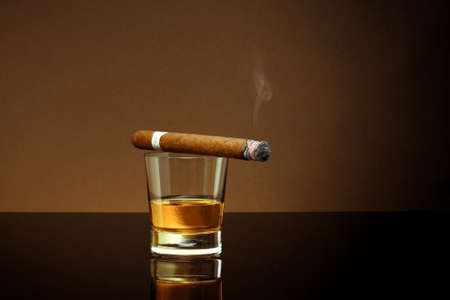Closed up view of glass of whiskey with cigar on top on color backの写真素材