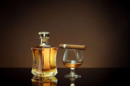 close up view of cigar, bottle of cognac and a glass aside on color back.の写真素材