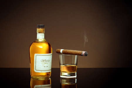 close up view of cigar, bottle of cognac and a glass aside on color back.の写真素材