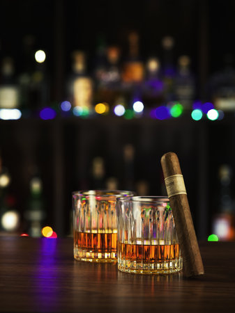 close up view of  two glasses with whiskey and cigar on color back.