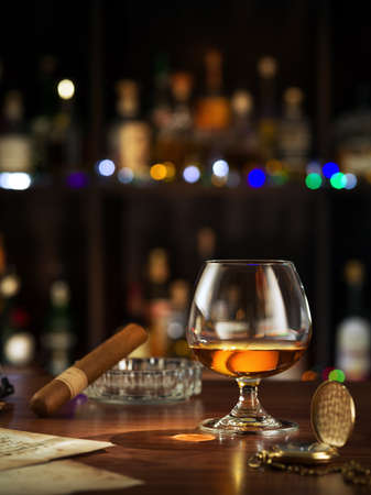 close up view of glass of cognac with cigar on top on color back.の写真素材
