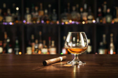 Closed up view of glass of cognac with cigar on color backの写真素材