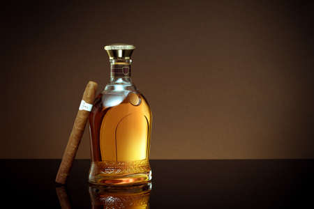 close up view of cigar and  bottle of cognac aside on color back.の写真素材