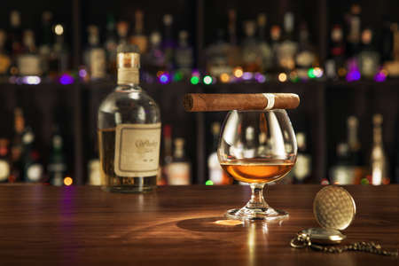 close up view of cigar, bottle of whiskey and a glass aside on color back.の写真素材