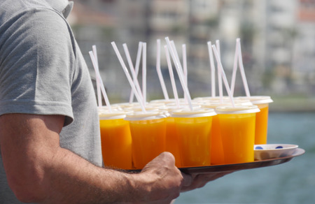 orange juice cups on tray in waiter hands at cafeの写真素材
