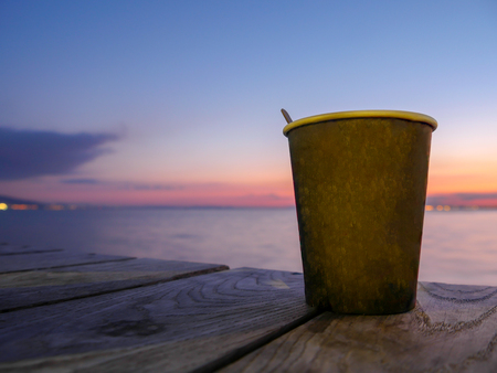 Paper tea or coffee cup, sunset sea background, early dark morning, coffee on sunrise or on sunsetの写真素材