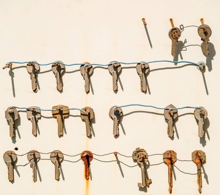 Many house keys hanging on a weathered wall.