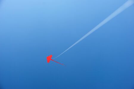 A red kite flying up high in the bright blue clear sky.の写真素材