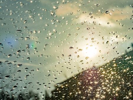 Wet window with rain drops and a cloudy sky outside background.