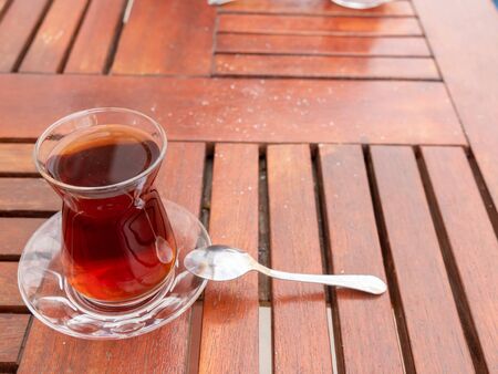 Turkish black tea glass with teaspoon on the wooden table. Turkish traditional drink.