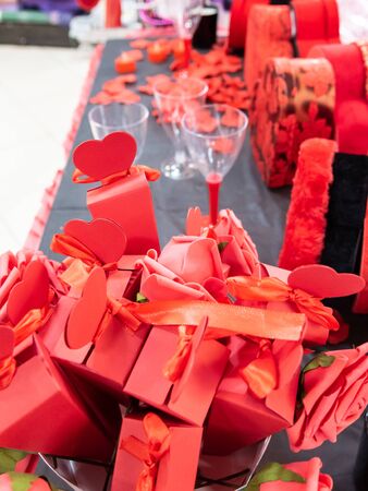 Close up of imitation or artificial red rose leaves, red heart shaped boxes and wine glasses background. Selective focus.の写真素材