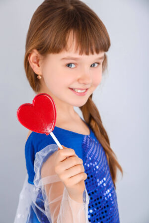 Beautiful child girl  holding a lollipop in the shape of a red heart valentines dayの写真素材