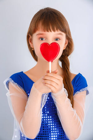 Beautiful child girl  holding a lollipop in the shape of a red heart valentines dayの写真素材