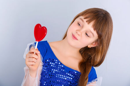 Beautiful child girl  holding a lollipop in the shape of a red heart valentines dayの写真素材