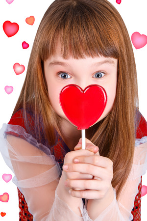 Beautiful child girl  holding a lollipop in the shape of a red heart valentines dayの写真素材