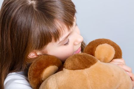 A portrait of a young pretty girl smiling and hugging her teddy bearの写真素材