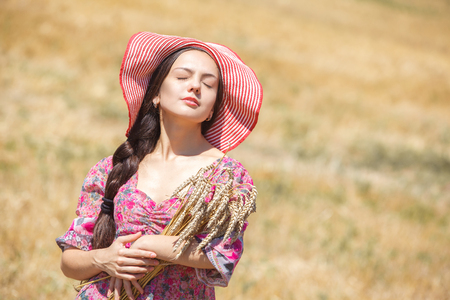Happy girl in hat on wheat field. Big hat and blowing long hairの写真素材