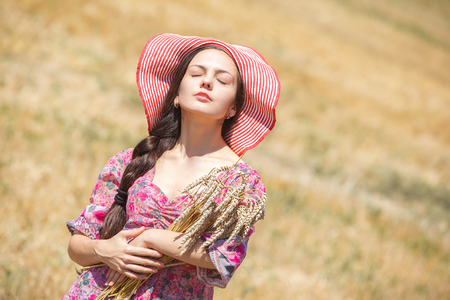Happy girl in hat on wheat field. Big hat and blowing long hairの写真素材