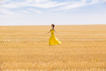 Young  woman in yellow dress in wheat fieldの写真素材