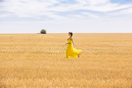Young  woman in yellow dress in wheat fieldの写真素材