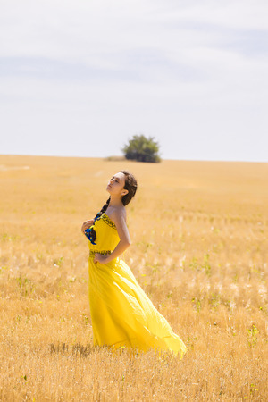 Young  woman in yellow dress in wheat fieldの写真素材