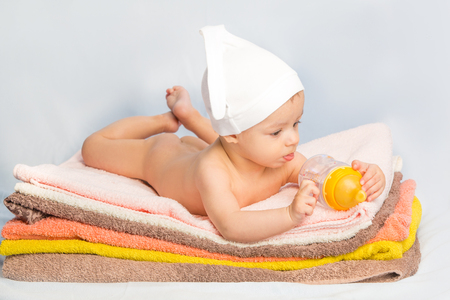baby on colorful towels stack. baby  holding milk from bottleの写真素材