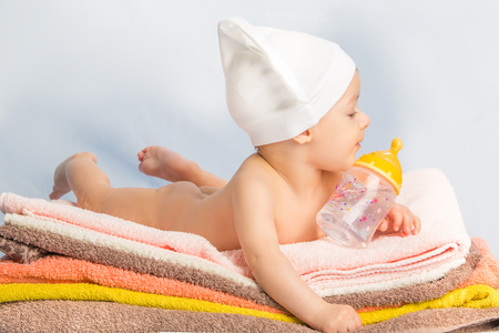 baby on colorful towels stack. baby  holding milk from bottleの写真素材