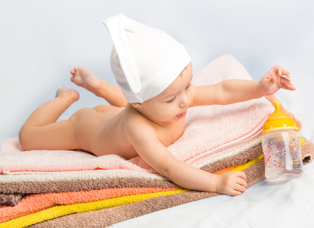 baby on colorful towels stack. baby  holding milk from bottleの写真素材