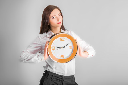 Portrait of beautiful young business woman holding in hands clock,  discipline and punctual concept on grey backgroundの写真素材