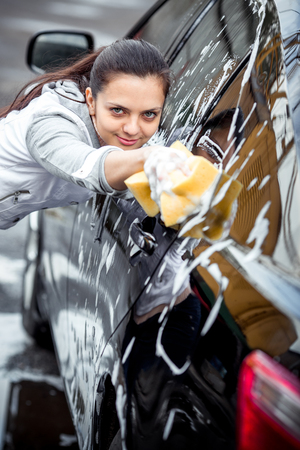 outdoor car wash with yellow sponge. Beautiful girl washes the carの写真素材