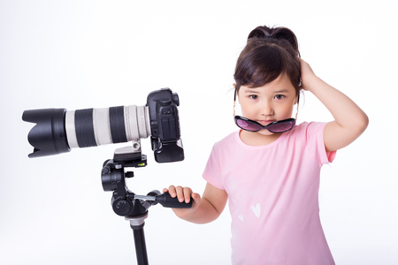 portrait of little cute girl holding a modern professional photo camera on tripod. child photographsの写真素材