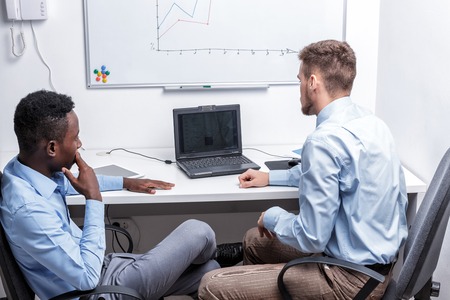 two managers sitting at a table and look at the diagram on the whiteboard in the officeの写真素材