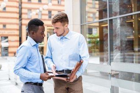 African American businessman and a Caucasian businessman discussing and looking at the documents on city backgroundの写真素材