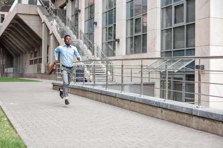 Young African American businessman with briefcase running down the street of the city. late for workの写真素材