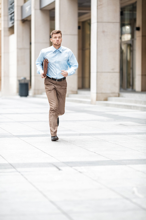 Young businessman with a briefcase running in a city street. Hurrying to work.の写真素材