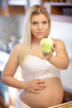 beautiful pregnant woman holding green Apple and smiling. focus on Appleの写真素材