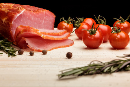Piece of smoked Ham with some fresh mushrooms, tomato, garlic and herbs on wooden Board on black backgroundの写真素材