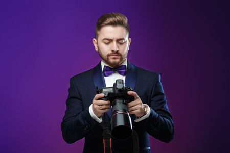 successful professional photographer in tuxedo use DSLR digital camera on dark backgroundの写真素材