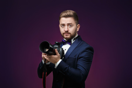 successful professional photographer in tuxedo use DSLR digital camera on dark backgroundの写真素材