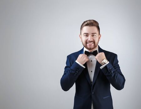 Handsome man in tuxedo and bow tie looking at camera. Fashionable, festive clothing. emcee on grey backgroundの写真素材