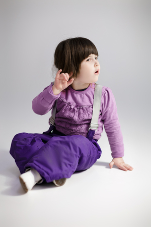 little cute girl in purple clothes trying to hear  on grey backgの写真素材