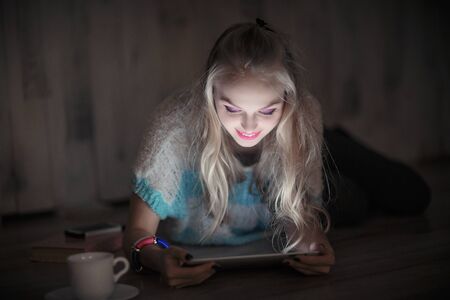 beautiful young blonde woman looks and reads on tablet and drinkの写真素材