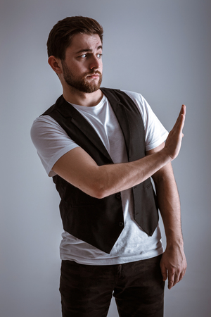 young handsome man with beard in white shirt and black waistcoat shows gesture stopの写真素材