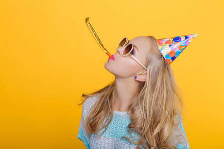 portrait of funny blond woman in birthday hat and blue shirt on yellow background. Celebration and party.の写真素材