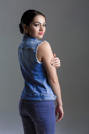 portrait of sexy young brunette woman in denim vest on grey background.の写真素材