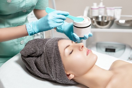 beautician applies face cream on beautiful young woman in Spa salon. cosmetic procedure skin care.の写真素材