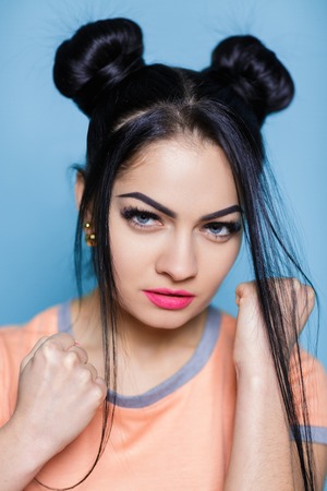 evil portrait of young brunette woman with fists on blue background