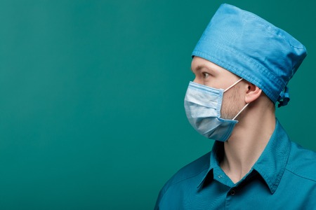 profile portrait of male surgeon in mask on blue background, close up. copy spaceの写真素材